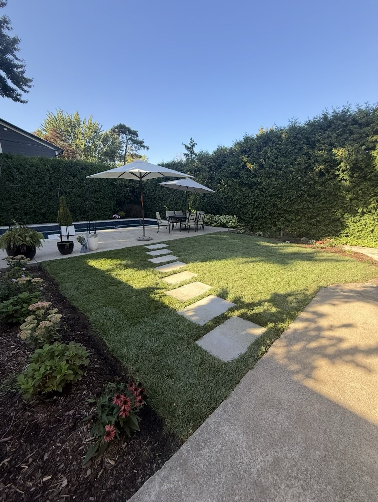 Backyard with fresh lawn, stepping-stone walkway and garden beds by CBR Property Care